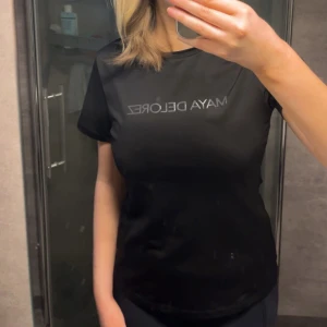 Svart t-shirt från Maya Delorez - Snygg svart t-shirt från Maya Delorez med tryck på bröstet och längs ryggen. Perfekt för en stilren look. Kortärmad och i ett bekvämt material.