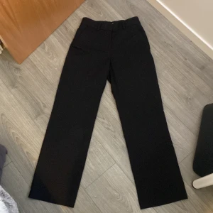 Svarta kostymbyxor från H&M - Snygga svarta kostymbyxor från H&M med en klassisk rak passform. Byxorna har hällor för bälte och diskreta fickor baktill. Perfekta för en stilren look.