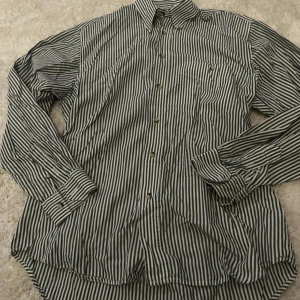 Randig skjorta från Joy Boy - Snygg randig skjorta från Joy Boy. Skjortan har långa ärmar och knappar framtill. Perfekt för en stilren look. Storlek M, 38