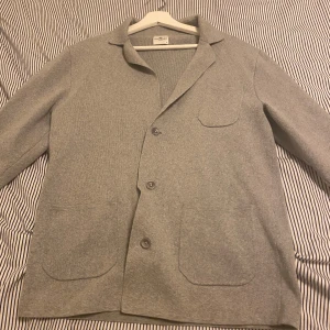 Grå kofta från John Henric - Säljer en stilren grå kofta från John Henric. Koftan har en klassisk krage och knappar framtill. Den är utrustad med två fickor på framsidan för extra funktionalitet. Perfekt för en elegant och avslappnad look. Säljer för ett billigt pris för 499kr! ✅