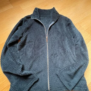 Mörkblå fleecejacka med dragkedja - Säljer en mysig mörkblå fleecejacka med dragkedja. Perfekt för kyliga dagar med sin mjuka och varma textur. Jackan har en hög krage och långa ärmar för extra komfort.