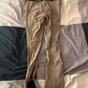 Beige ridbyxor från CRW - Säljer ett par beige ridbyxor från CRW med svarta detaljer och elastisk midja. Byxorna har dragkedja och knappar framtill samt förstärkta sömmar för extra hållbarhet. Perfekta för utomhusaktiviteter. Aldrig använda!