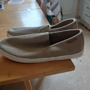 Beige slip-on sneakers - Säljer ett par bekväma beige slip-on sneakers med nätmaterial från Gant. Skorna har en vit sula och är perfekta för en avslappnad stil. De är lätta att ta på och av, vilket gör dem praktiska för vardagsbruk.
