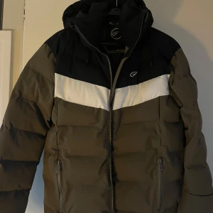 Svart och olivgrön pufferjacka från Five Seasons - Säljer en svart och olivgrön pufferjacka från Five Seasons. Jackan har en vit rand över bröstet och dragkedja framtill. Den är designad för komfort med vattenresistens och andningsförmåga. Perfekt för kyliga dagar och skidåkning