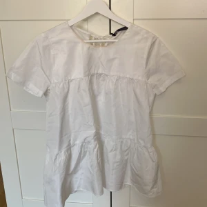 Vit blus/topp från Zara - Säljer en söt vit blus från Zara i storlek XS. Blusen har korta ärmar och en knytning i ryggen för en extra detalj. Perfekt för en stilren look. Sminkfläck vid halsen men går säker bort enkelt. Pris går att diskutera.