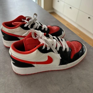 Nike Air Jordans i rött, svart och vitt - Snygga Nike Air Jordans i en cool färgkombination av rött, svart och vitt. Skorna har en klassisk design med snörning och den ikoniska Nike-loggan på sidan. Perfekta för dig som vill ha en stilren och sportig look.