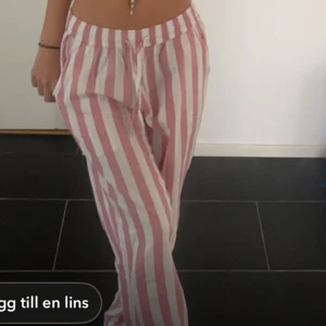 Randiga byxor i rosa och vit - Säljer ett par bekväma byxor med rosa och vita ränder. De har en loose passform och är perfekta för en avslappnad stil. Byxorna har en elastisk midja med snörning för extra komfort.