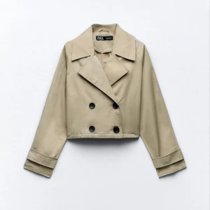 Beige croppad kavaj från Zara - Säljer en snygg beige croppad kavaj från Zara med dubbelknäppning och stora svarta knappar. Jackan har en klassisk krage och långa ärmar, perfekt för en stilren look.