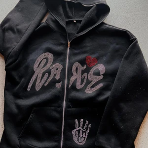 Svart hoodie med tryck - Säljer en svart hoodie med dragkedja upp över luvan, oklar på märket men den är jävligt fet. Öppen för bud och byten, den är lite nopprig. Sitter som L 