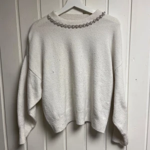 Vit tröja med pärldetaljer - Säljer en stilren vit tröja med pärldetaljer runt halsen. Tröjan har en avslappnad passform med långa ärmar och ribbade kanter. Perfekt för en elegant och mysig look.