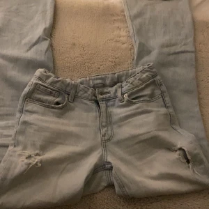Ljusblå jeans med slitningar - Snygga ljusblå jeans med slitningar på knäna. De har en klassisk femficksdesign och en knappgylf. Perfekta för en avslappnad stil.