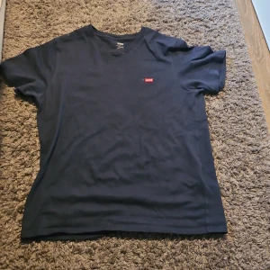 Mörkblå t-shirt från Levi's - Säljer en klassisk mörkblå t-shirt från Levi's med en liten röd logga på bröstet. Perfekt för en avslappnad stil. Tillverkad i Vietnam.