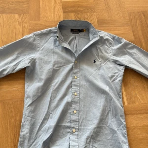 Blå skjorta från Polo Ralph Lauren - Tja! 🌊 Säljer en nice blå skjorta från Polo Ralph Lauren. Skjortan har en klassisk krage och knappar framtill. Perfekt nu inför sommaren 🤩. Storlek S men passar nog bättre till M. Har tyvärr inte kommit till användning pågrund av den större storleken.