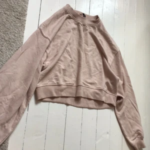 Rosa croppad tröja från Divided - Säljer en rosa croppad tröja från Divided med broderad text 'Smile' på framsidan. Tröjan har långa ärmar och en ribbad halsringning. Perfekt för en avslappnad stil. Har dock tre fläckar på framsidan.