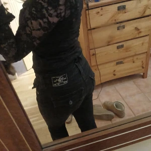 True Religion jeans  - Svarta bootcut jeansbyxor från True Religion med knappar på bakfickorna och en klassisk femficksdesign. Byxorna har en midwaist passform och slutar en bit under navlen. Köpte på plick för 1000kr. Inga defekter mer än nere vid benen men de är fortfarande hela. Tvättade innan frakt, kontakta för frågor!🥰