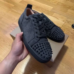 Gråa loubs med spikar - Snygga gråa loubs i mocka med nitar på tån och en ikonisk röd sula. Skorna har snörning och en stilren design som sticker ut.