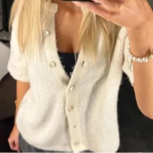 Vit stickad blus med pärlknappar - Superfin vit stickad blus med korta ärmar och snygga pärlknappar framtill. Den har en mjuk och fluffig känsla och passar perfekt till jeans eller kjol. Enkel men ändå elegant look.