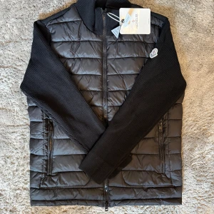 Moncler Cardigan  - Exklusiv cardigan från Moncler i svart med quiltad front och stickade ärmar. Klassisk och stilren design med hög premiumkvalitet. Perfekt balans mellan en lätt jacka och en lyxig kofta.  ♦️ Helt ny – med originaltag kvar ☑️ ⚜️ Storlek M – normal passform ☑️ ♦️ Lyxig design – både funktionell & tidlös ☑️  📦 Snabb leverans & säker affär 