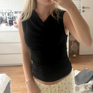 Svart glittrig ärmlös topp - Snygg svart ärmlös topp med glittrigt tyg och draperad halsringning. Perfekt för dig som vill sticka ut med lite extra shine. Toppens material är stretchigt och sitter tajt mot kroppen för en smickrande passform. Aldrig använd med lappen kvar!🖤