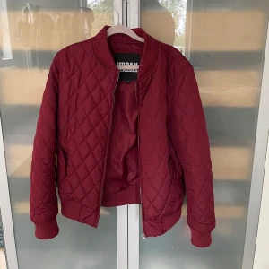 Quiltad vinröd bomberjacka Urban Classics - Säljer en vinröd quiltad bomberjacka från Urban Classics. Jackan har ribbade muddar, dragkedja framtill och ett snyggt rutmönster. Perfekt för dig som vill ha en stilren och bekväm jacka med streetkänsla. Skriv om du undrar något 💞