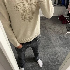 Beige stickad tröja från Morris - Snygg beige stickad tröja från Morris med klassiskt tryck och emblem på bröstet. Tröjan har rund halsringning, ribbade muddar och lång ärm. Perfekt för dig som gillar stilren och clean stil.