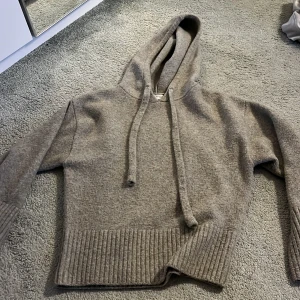 Grå stickad hoodie från Zara - Mysig grå hoodie från Zara i stickat material med huva och snörning. Tröjan har bred ribbad mudd nedtill och långa ärmar.