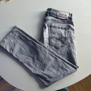 Grå jeans från Replay - Snygga ljusgrå jeans från Replay med klassisk femficksdesign och diskret sliten detalj på ena benet. Jeansen har raka ben och är tillverkade i mjukt denimtyg som ger en avslappnad vibe. Perfekta för dig som gillar en stilren men ändå cool look.