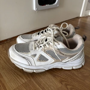 Vita chunky sneakers med meshdetaljer - Säljer ett par vita chunky sneakers med grå meshdetaljer och beige inslag. Skorna har snörning och en rejäl sula som ger en sportig vibe. Perfekta för dig som gillar streetstyle och vill ha bekväma skor till vardagen. Nyskick då de är använda endast två gånger då de är förstora