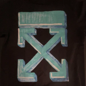 Svart Off-White t-shirt med blått tryck - Svart t-shirt från Off-White i bomull med stort blått och turkost grafiskt tryck på ryggen och liten Off-White-logga på bröstet. Klassisk passform och korta ärmar. Perfekt för dig som gillar streetwear och vill sticka ut.