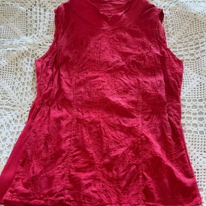 Vintage  broderad topp - Snygg röd topp med broderade detaljer och hög krage. Ärmlös modell i linnetyg. Passformen är något större med möjlighet att sy in sidorna om man så önskar. Toppen har vackert broderi på framsidan, se bild 4. Köpt på second hand och står inget märke men tillverkad i Italien, se bild 5.