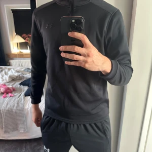 Svart half zip tröja från Under Armour - Säljer en svart långärmad tröja från Under Armour med half zip och broderad logga på bröstet. Tröjan är i loose fit och tillverkad i ett mjukt, värmande material som passar perfekt för träning eller kyligare dagar. Under Armour Coldgear