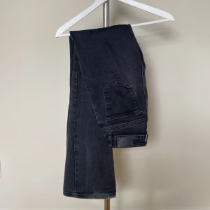 Svarta raka jeans från Gina - Säljer ett par svarta jeans från Gina med klassisk femficksdesign och raka ben. Jeansen har en mörk tvätt och är tillverkade i mjukt denimtyg som sitter snyggt och bekvämt. Perfekta för dig som gillar en stilren och tidlös look.