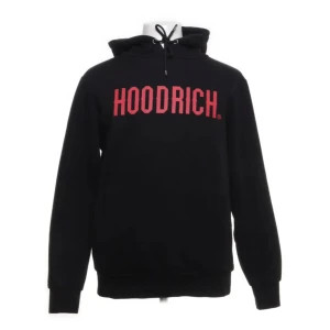 Svart hoodie från Hoodrich med röd text - Svart hoodie från Hoodrich med stor röd logga framtill på bröstet. Klassisk huva med snörning och långa ärmar. kan skicka flera bilder på tröjan