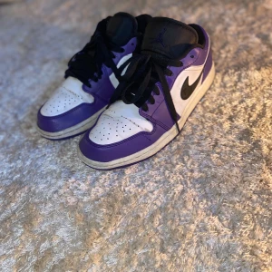 Nike Air Jordan 1 Low Court Purple - Säljer ett par Nike Air Jordan 1 Low i färgen Court Purple. Skorna har en snygg kombination av lila och vitt skinn med svarta detaljer och snörning. Klassisk svart swoosh på sidan och perforerad tåbox för extra stil. Perfekta för dig som vill sticka ut med dina sneakers. En sula är bytt på grund av att den gick sönder men ingenting man märker. En liten defekt på sulan (se bild) annars är dom i väldigt bra skick. 