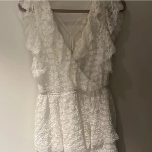 Vit spetsklänning från Nelly XS - Supersöt vit kortklänning från Nelly i spets med volanger och omlottkänsla. Klänningen har knyt i ryggen och är ärmlös med romantiska detaljer. Perfekt för sommarens alla tillfällen! Pris kan diskuteras 🩷🤗🥂