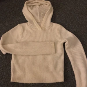 Vit stickad hoodie med huva - (Nypris 300kr)Mysig vit stickad hoodie med huva och ribbad struktur. Tröjan har långärmad design och är perfekt för kyliga dagar. Enkel och stilren look som passar till många outfits. 