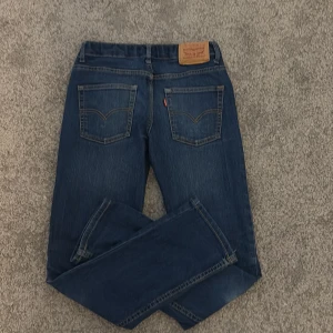 Levi's 511 Slim Jeans Blå Denim - Snygga Levi's 511 jeans i klassisk blå denim med slim fit. Jeansen har 4 fickor, guldfärgade sömmar och en ikonisk läderpatch bak i midjan. Perfekta för dig som gillar en smalare passform och tidlös stil.