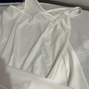 Vit långklänning med smala axelband - Säljer en elegant vit långklänning med smala axelband och enkel, stilren design. Klänningen har en mjuk och följsam känsla, perfekt för dig som gillar minimalistisk stil. Materialet känns svalt och lätt mot huden.