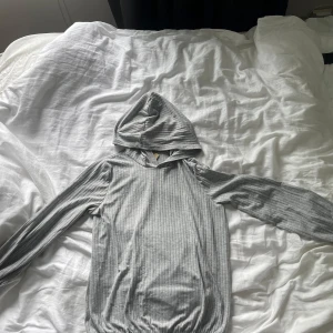 Grå ribbad hoodie från Boohoo - Säljer en ljusgrå ribbad tunn hoodie från Boohoo i storlek 36. Tröjan har långa ärmar, huva och är tillverkad i mjukt material som känns skönt mot huden. Perfekt för en chill och avslappnad look.