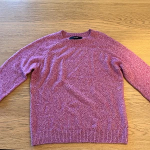 Rosa stickad tröja från Vero Moda - Mysig rosa stickad tröja från Vero Moda i storlek S. Tröjan har en klassisk rund halsringning, långa ärmar och ribbade muddar vid ärmslut och nederkant. Perfekt för lager-på-lager under kyliga dagar.