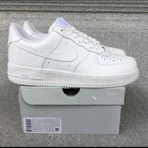 Nike Air Force 1 skor UTAN BOX!! - Klassiska Nike Air Force 1 sneakers i helvitt skinn med vit sula och diskret Nike-logga på sidan. Modellen har rund tå, snörning och perforerade detaljer på tån för extra ventilation. Perfekt för dig som gillar en clean och tidlös look. BOX KOMMER INTE MED!!
