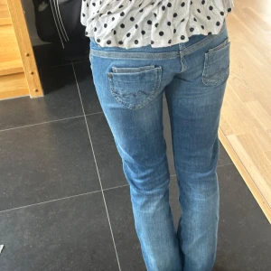 Blå jeans med raka ben - Säljer ett par klassiska blå jeans med raka ben och väldigt låg midja. Jeansen har dubbla knappar i midjan, fem fickor och snygga detaljer på bakfickorna. Perfekta till vardags och lätta att matcha med mycket! Köptes för ca 600kr och knappt använda! Från pepe jeans! 