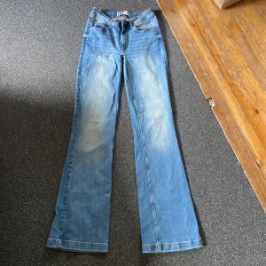 Blå bootcut jeans från JDY - Snygga ljusblå jeans från JDY med klassisk femficksdesign och bootcut-ben. Jeansen har normal passform och är tillverkade i jeansmaterial med lätt slitning på låren. Perfekta för dig som gillar en retroinspirerad look och vill ha ett par bekväma jeans med lite vidare ben. Har även sytt ner dom till lågmidjade. W26 och L34.
