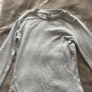 Grå långärmad tröja från H&M  - Säljer en enkel och stilren grå långärmad tröja från H&M Divided i storlek XS. Tröjan har rund hals och är gjord i mjukt bomullsmaterial med en lätt textur. Perfekt att matcha med jeans eller kjol för en chill look. Använd ett par gånger förra året men funkar som ny. Den sitter taight på kroppen och är basic. Säljer för 60kr, frakten blir mellan 20-40kr osäker. Köp inte på ”KÖP NU”, betalningen genomförs i chatten med Swish. 