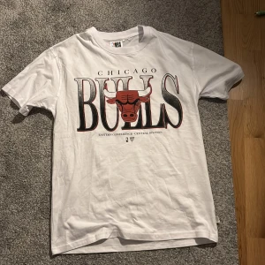 Vit Chicago Bulls t-shirt NBA XS - Snygg vit t-shirt från NBA med stort Chicago Bulls-tryck på framsidan. Klassisk passform med rund hals och korta ärmar. Perfekt för dig som gillar basket och vill ha en sportig stil. Tillverkad i mjuk bomull.