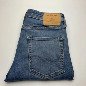 Jack & Jones jeans  - Snygga blå jeans från Jack & Jones med klassisk femficksdesign och ljus tvätt. Jeansen har bruna kontrastsömmar och en läderpatch bak i midjan. Perfekta för dig som gillar en enkel och stilren look.