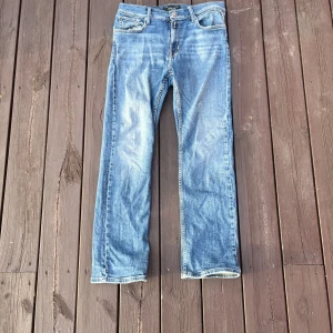 Blå raka jeans från Replay - Säljer ett par klassiska blå jeans från Replay med raka ben och snyggt slitna detaljer. Jeansen har fem fickor, normal passform och är tillverkade i bomull. Perfekta för dig som gillar en tidlös och avslappnad look.