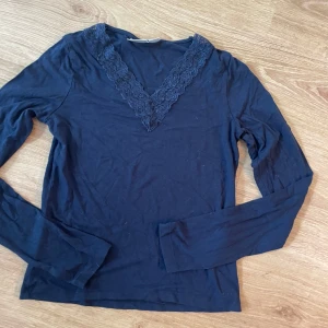 Mörkblå långärmad topp med spets - Supersnygg mörkblå långärmad topp från Gina Tricot med v-ringning och dekorativ spets runt halsen. Perfekt att styla med jeans eller kjol för en trendig look. Mjuk och skön i bomullsmix.