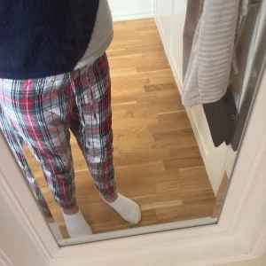 Röd-rutiga mjukisbyxor med snörning - Säljer ett par sköna mjukisbyxor i röd, vit och grön rutig design. Byxorna har snörning i midjan och är tillverkade i mjukt bomullstyg. Perfekta för chill dagar hemma eller när du vill vara extra bekväm.