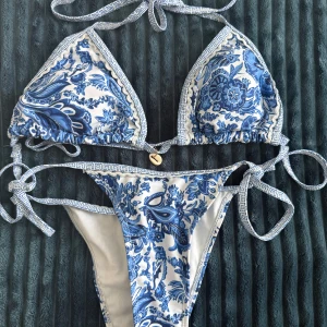 Blåvit blommig bikini med snörning - Superfin bikini med blått och vitt blommönster och snygga knytband i sidorna och nacken. Triangeltopp med dekorativt snäcksmycke framtill. 